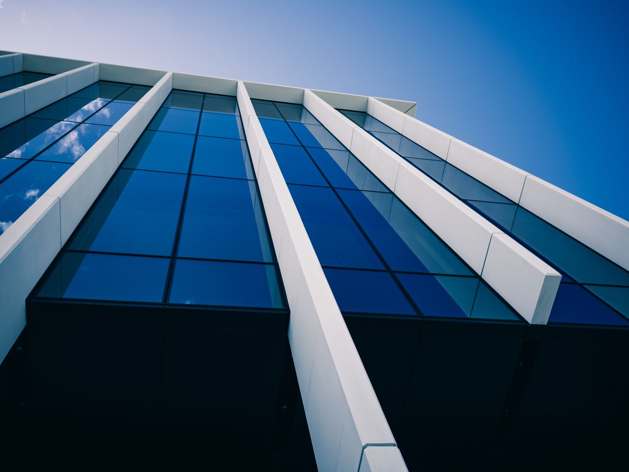 Services Low-angle view of a modern glass building against a clear blue sky, showcasing bold architectural lines.