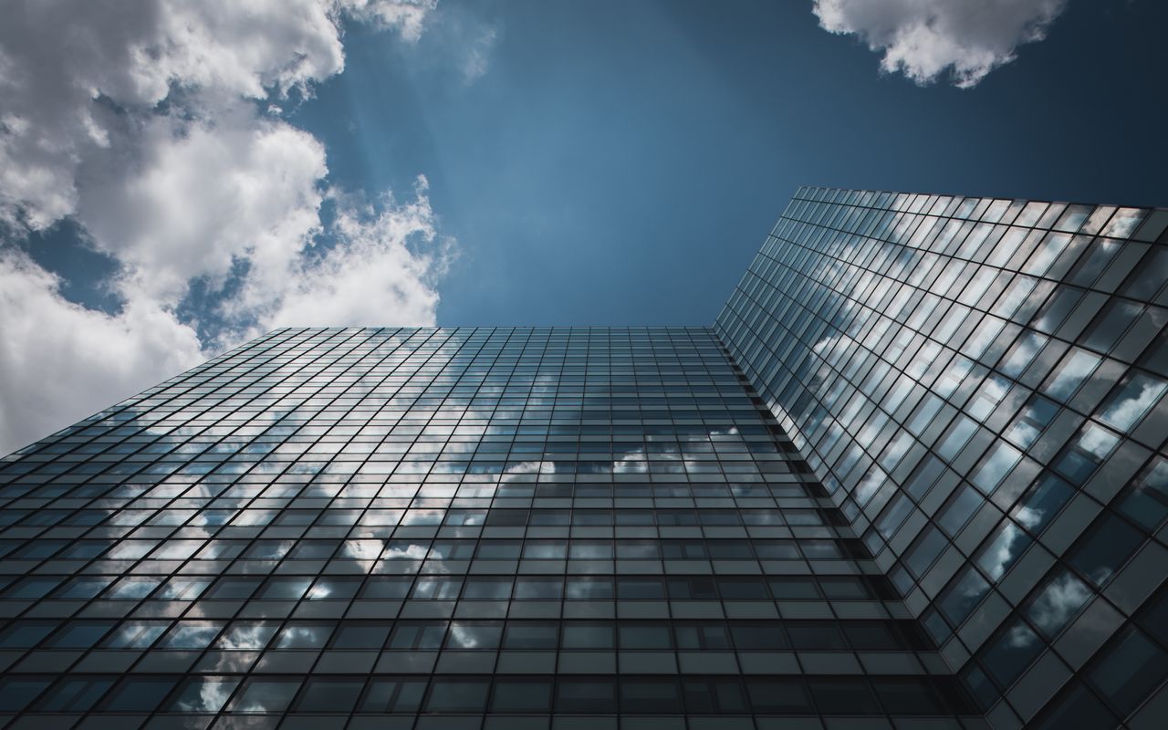 Services Low angle view of a glass skyscraper in Hamburg reflecting clouds in a clear sky.